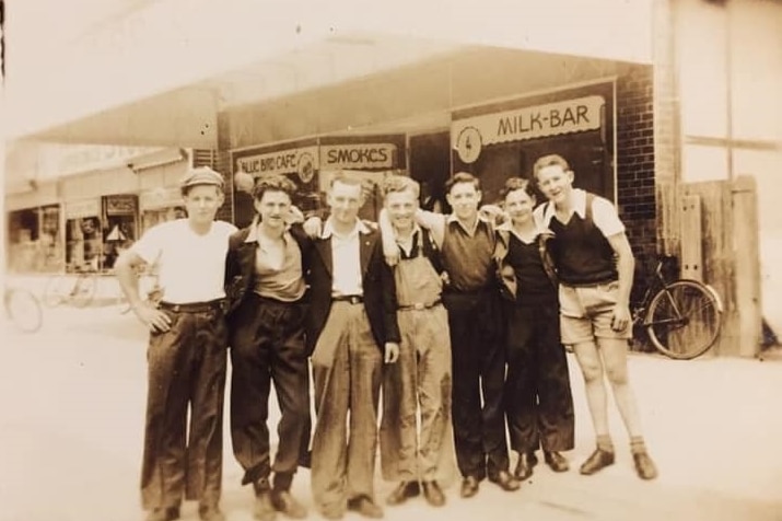 A sepia photograph showing a group of smiling people outside a cafe.