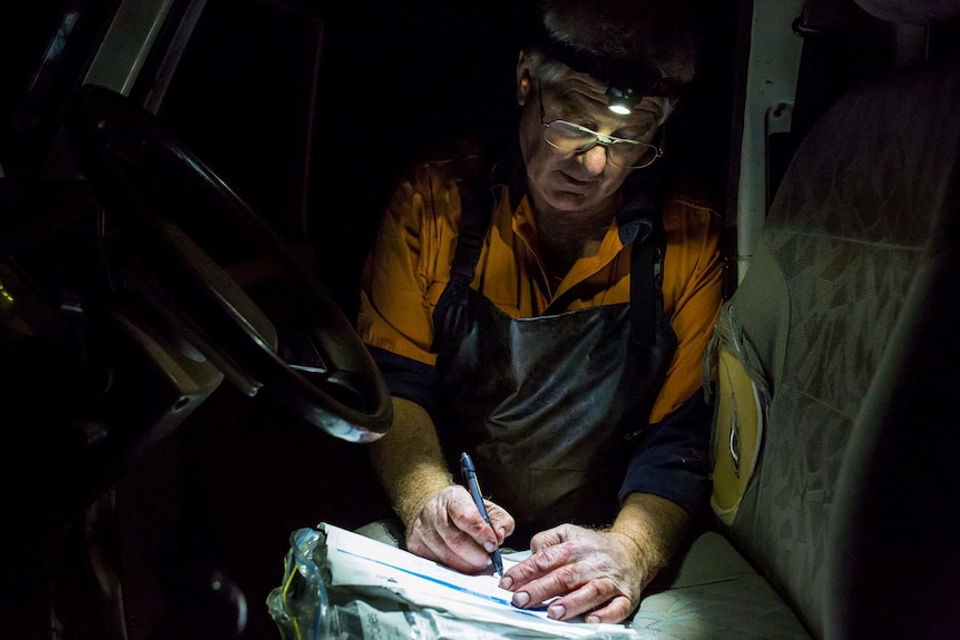 With an ear plug visible in one ear and red-stained hands, Glenn Cole does paperwork on the driver's seat of his truck.
