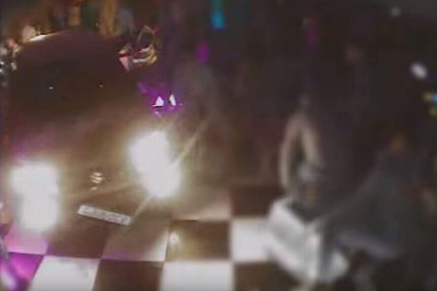 Blurry imagery of a car on a dancefloor, with people attempting to get out of the way.