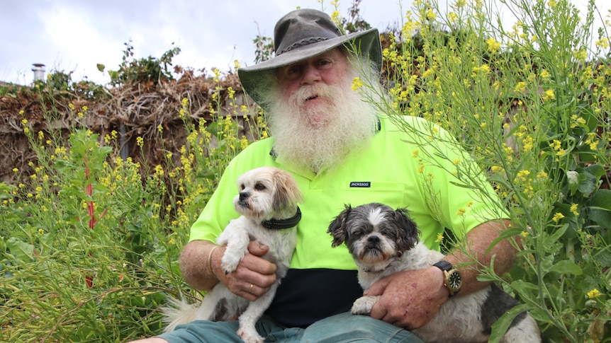 Pete Richards holds two dogs in front of garden bed.