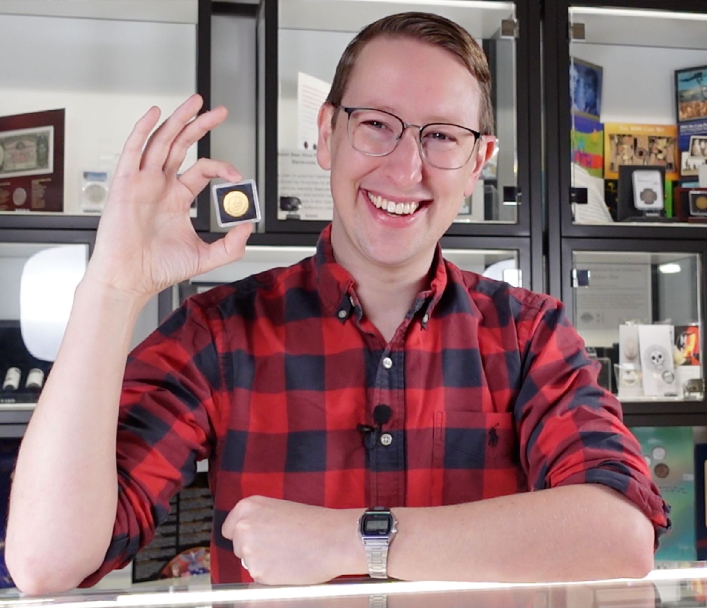 Um homem de óculos e camisa xadrez vermelha segurando uma moeda velha em uma caixa.