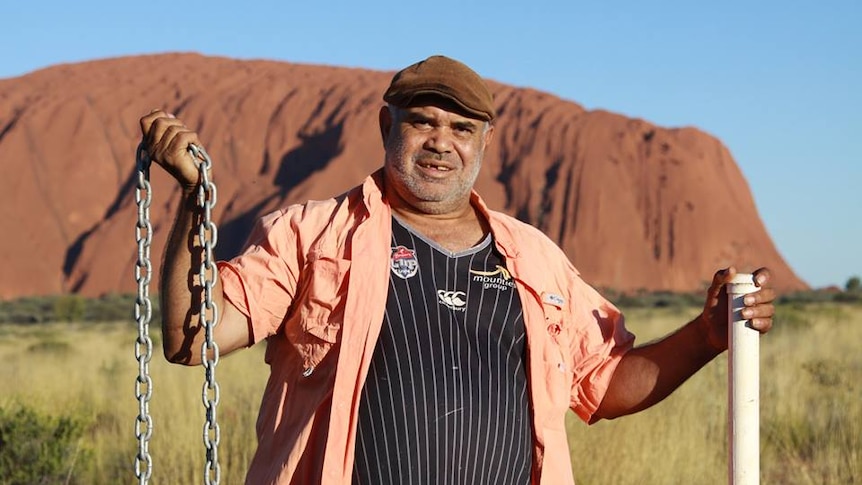 An Aboriginal man holds a chain in front of Uluru.