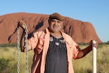An Aboriginal man holds a chain in front of Uluru.
