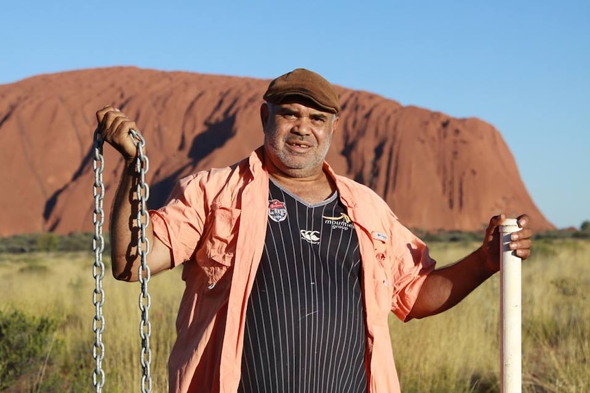 An Aboriginal man holds a chain in front of Uluru.