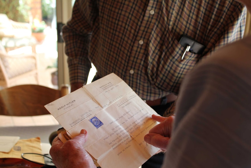 A woman holds a typed letter whilst a man looks on in the background.