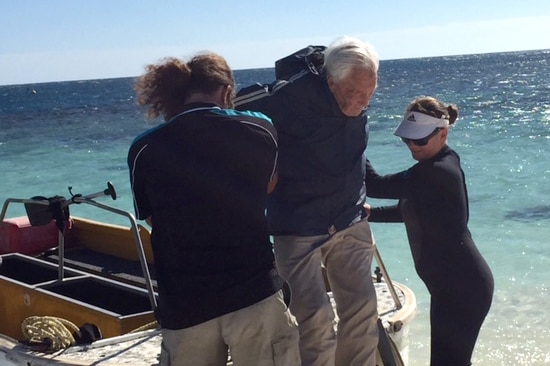 David Goodall being helped off a boat by two people.