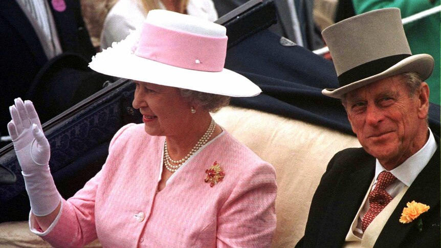 Queen Elizabeth II waves and Prince Philip smiles as they ride in an open carriage in 1997.