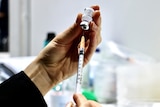 A close-up shot of someone's hands filling a syringe with the Pfizer COVID-19 vaccine.