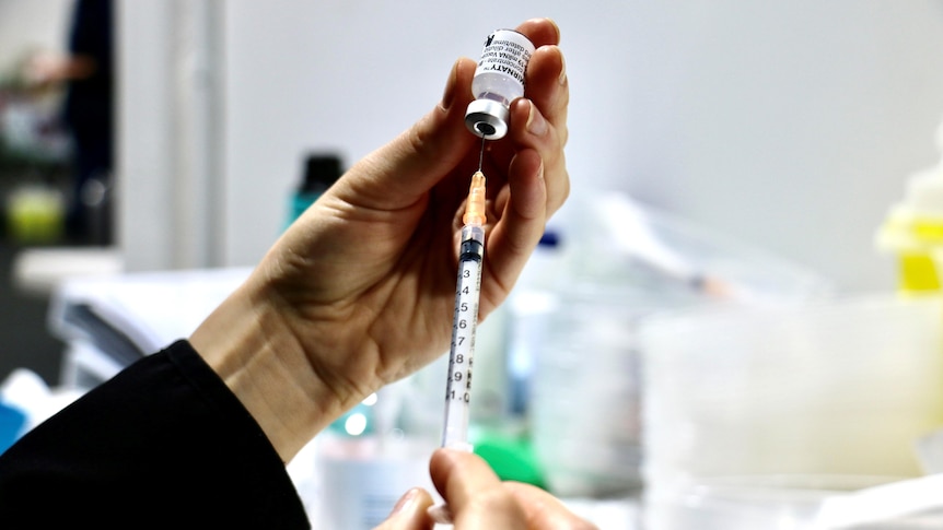 A close-up shot of someone's hands filling a syringe with the Pfizer COVID-19 vaccine.