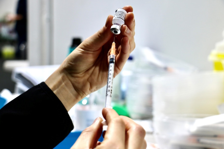 A close-up shot of someone's hands filling a syringe with the Pfizer COVID-19 vaccine.