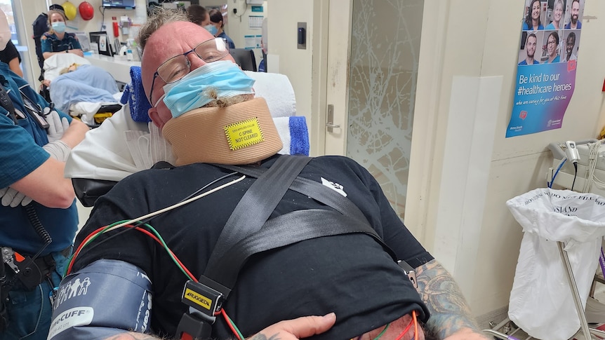 An image of Steve Whiteley in a hospital bed wearing neck brace and cords poking out under his shirt