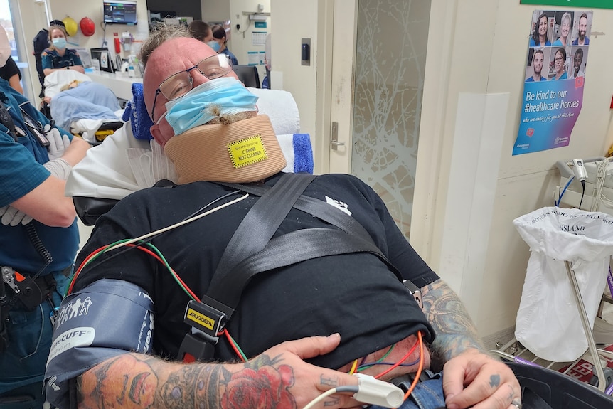 An image of Steve Whiteley in a hospital bed wearing neck brace and cords poking out under his shirt