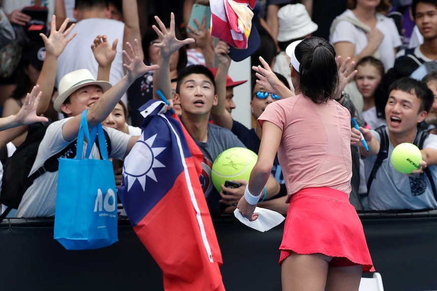 A tennis player (back to camera) throws her towel to spectators on the other side of the barrier.