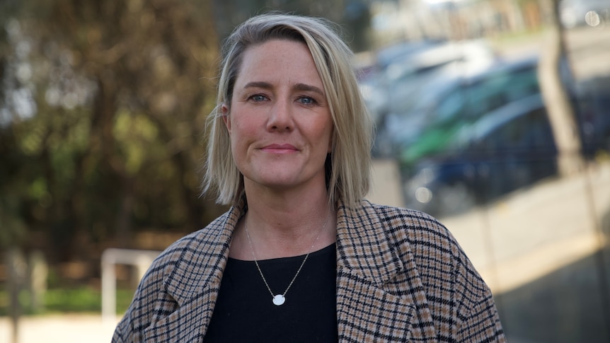 Woman with short blonde hair wearing a black shirt and checked jacket.