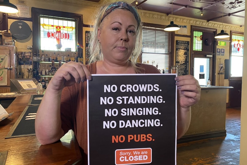 A woman holding a sign that says no crowds, no standing, no singing, no dancing, no ads
