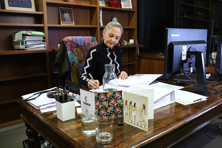 a woman holding a pen writing and sitting behind a desk