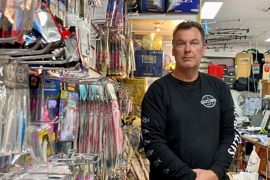 A man stands in his tackle shop surrounded by rods and bait.