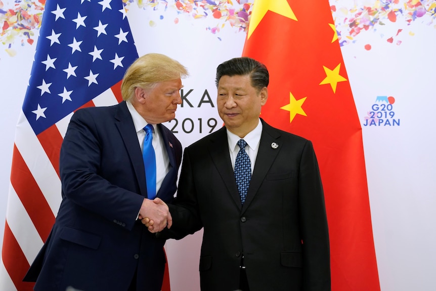 Donald Trump and Xi Jinping shake hands while standing in front of the flags of their respective nations.