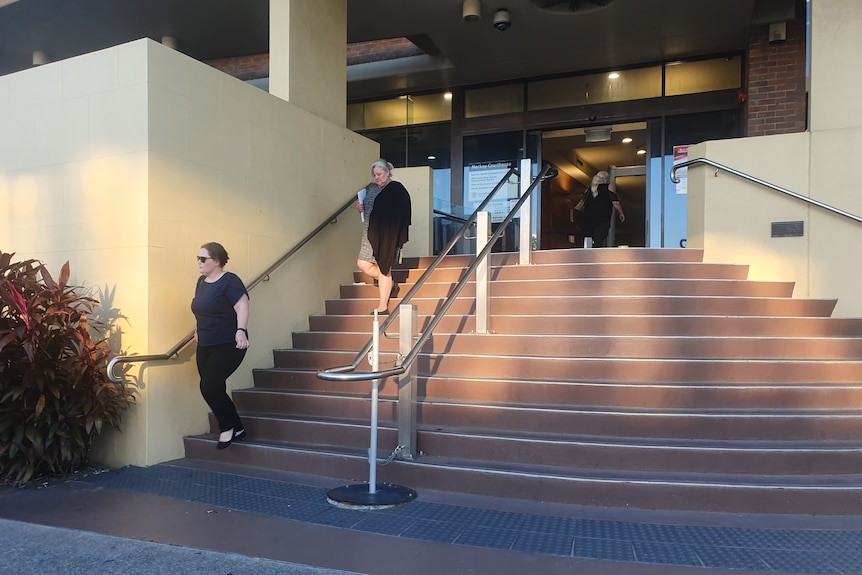 two woman walk down the stairs of a cream-coloured court house building