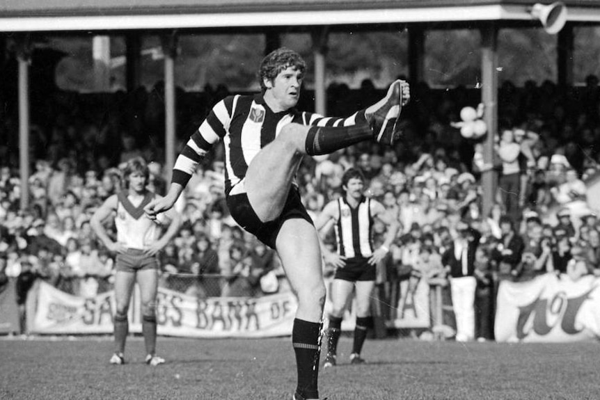 A black and white photo of a man in a stripy jumper kicking a football.