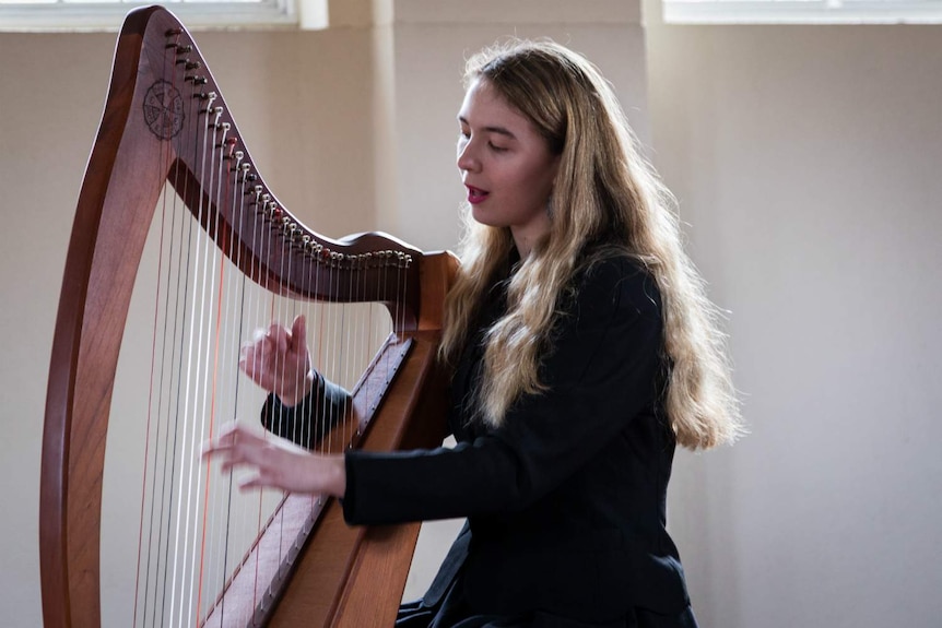 Amelia Le Plastrier plays the harp in a sunlit room.