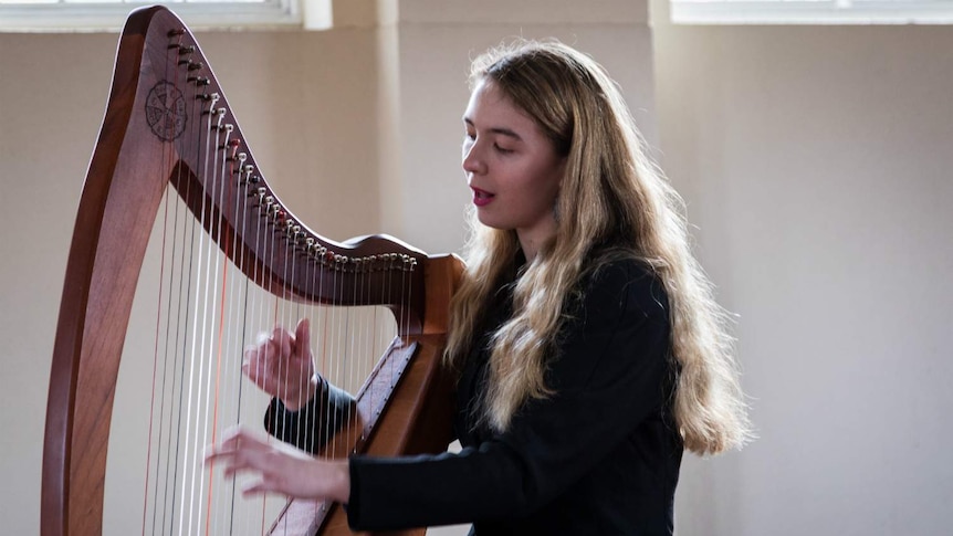 Amelia Le Plastrier plays the harp in a sunlit room.