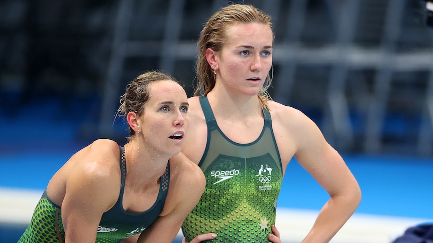 Emma McKeon bends forward as Ariarne Titmus stands beside her during a swimming relay.