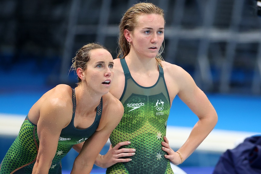 Emma McKeon bends forward as Ariarne Titmus stands beside her during a swimming relay.