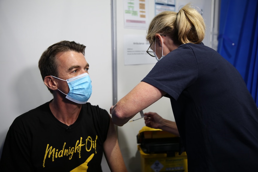 Michael Rowland wears a Midnight Oil shirt as he gets a vaccine in the arm.