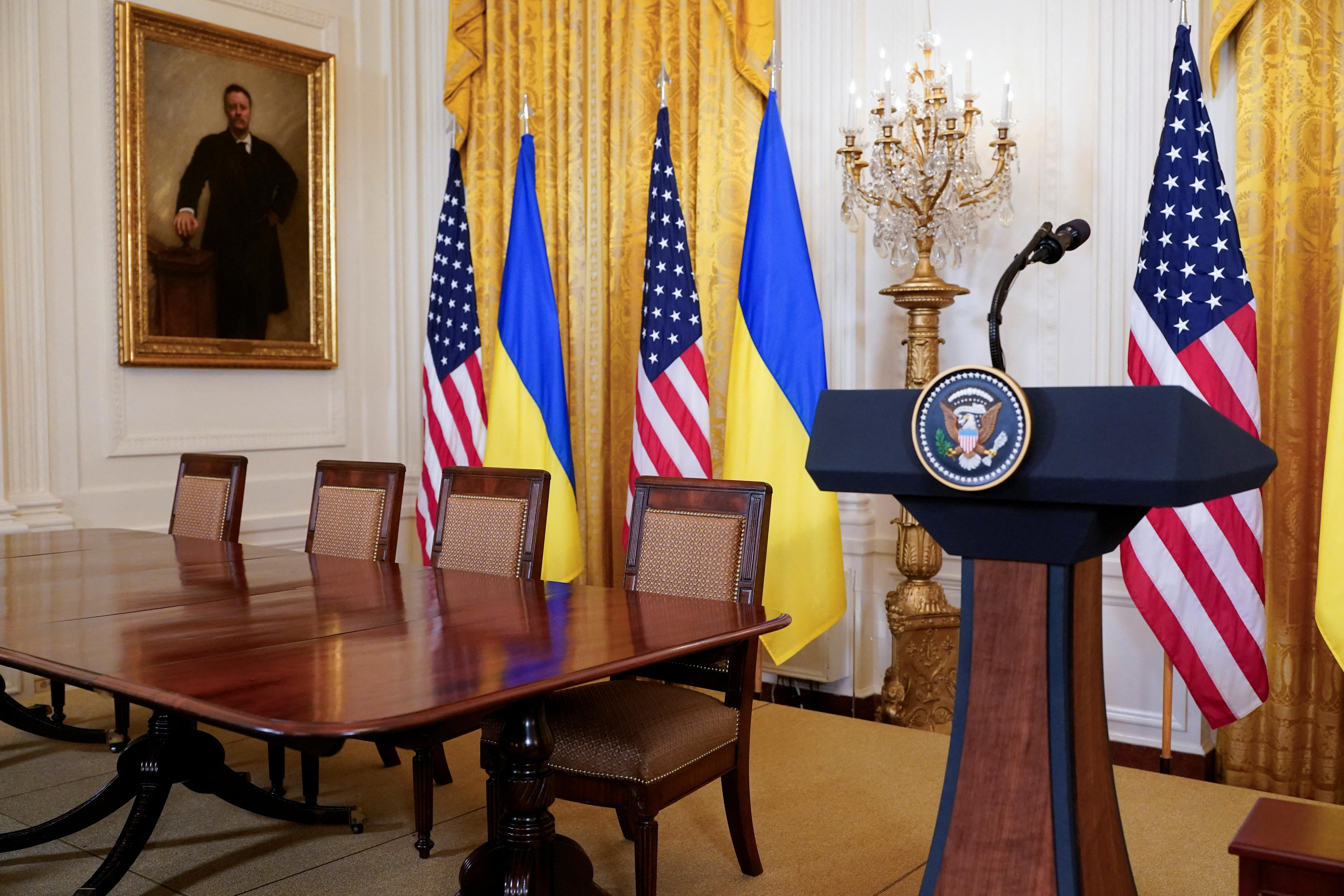 An empty US presidential lectern and table with the Ukrainian and US flags, in a White House room.