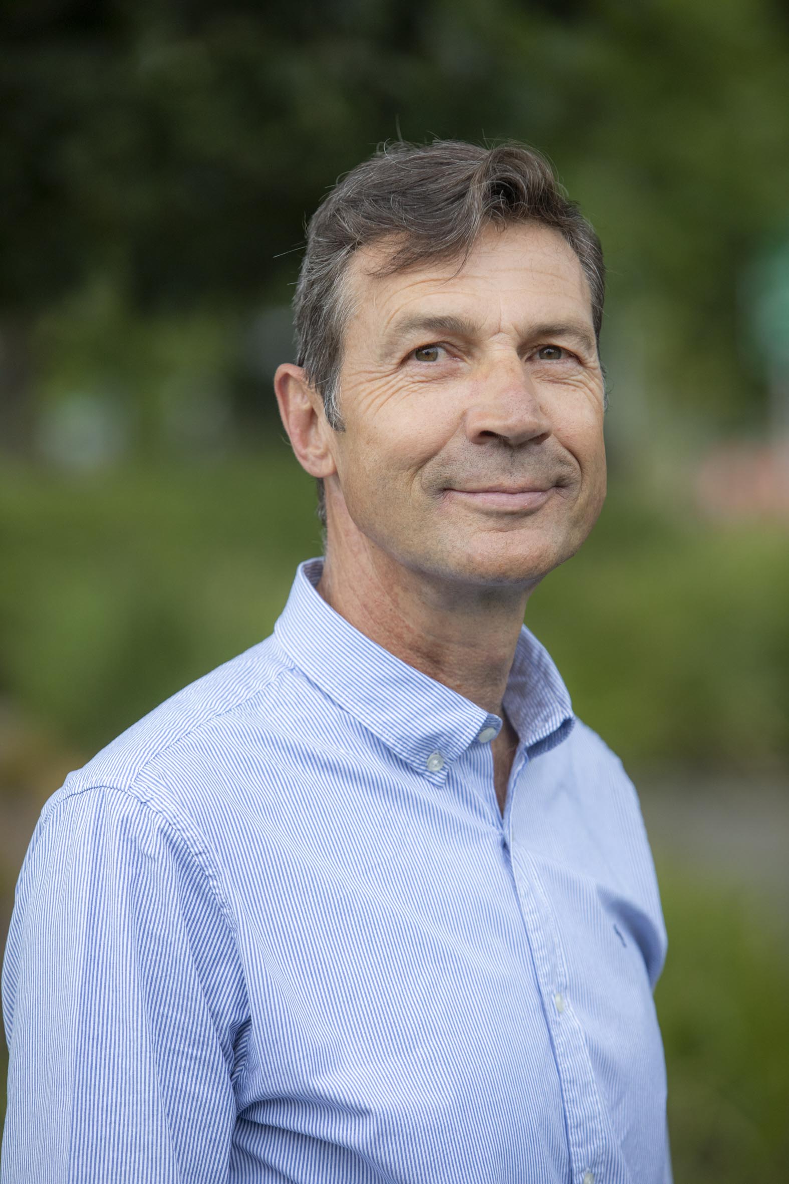 um homem sorrindo para a câmera contra um fundo verde desfocado