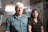 Tony and Leanne Nesci, a middle-aged couple, are sitting at a table in a ktichen and looking seriously into the camera.