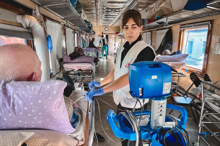 A nurse checks a patient and monitoring device in a train lined with hospital trolley beds.