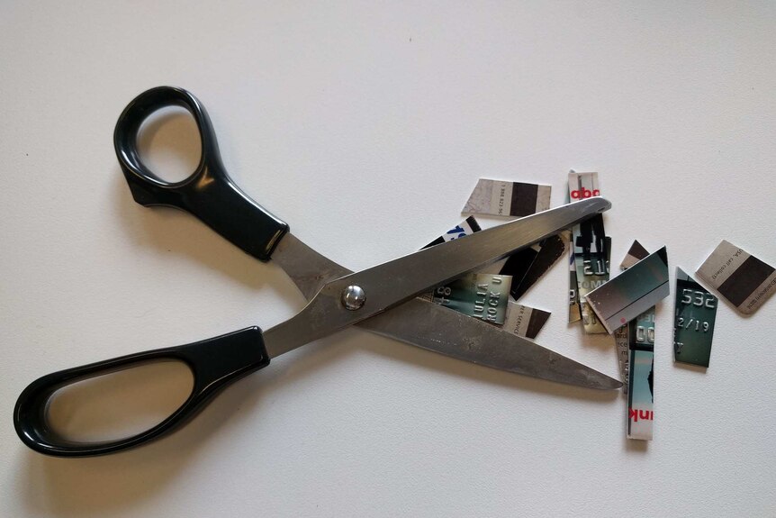 A pair of black scissors besides a credit card that has been cut up into tiny pieces