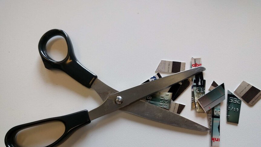 A pair of black scissors besides a credit card that has been cut up into tiny pieces