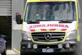 An ambulance in a carpark during the day with someone at the wheel.