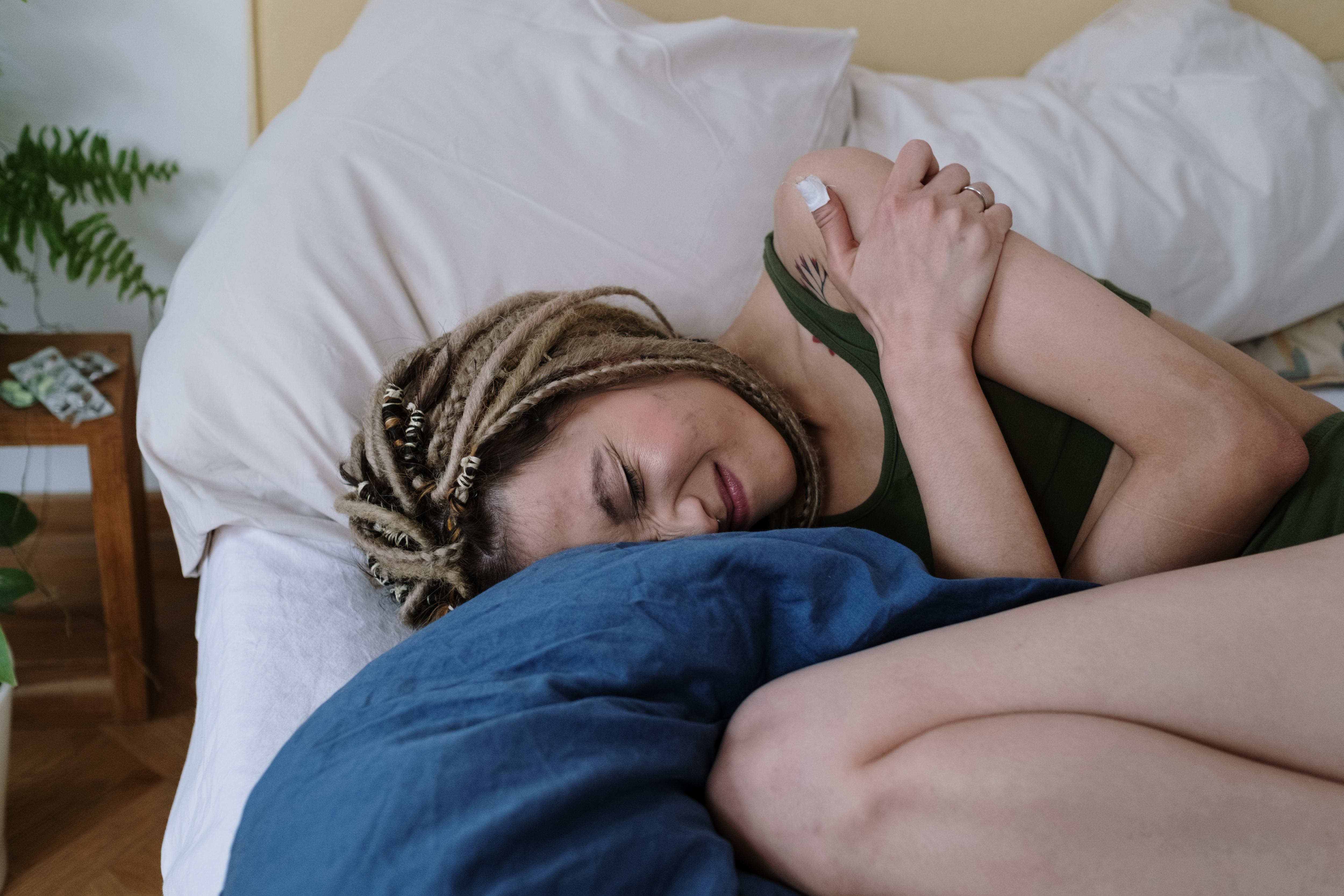 Woman curling up on bed while clutching her stomach