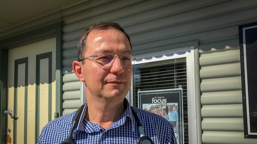 A Doctor with stethoscope draped over his shoulders standing outside his surgery.