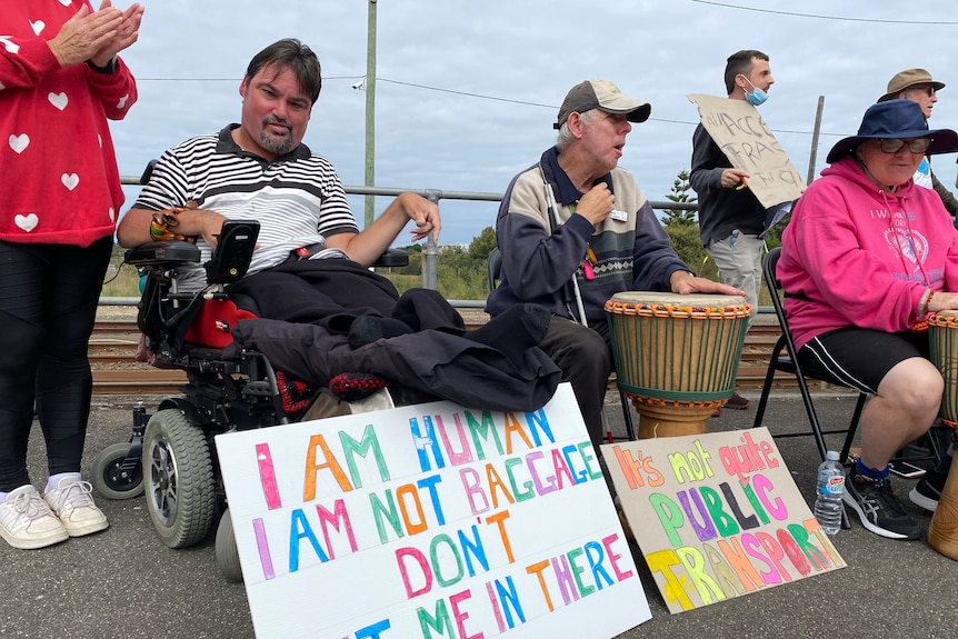 A man in a wheelchair with a sign reading "I am human" 
