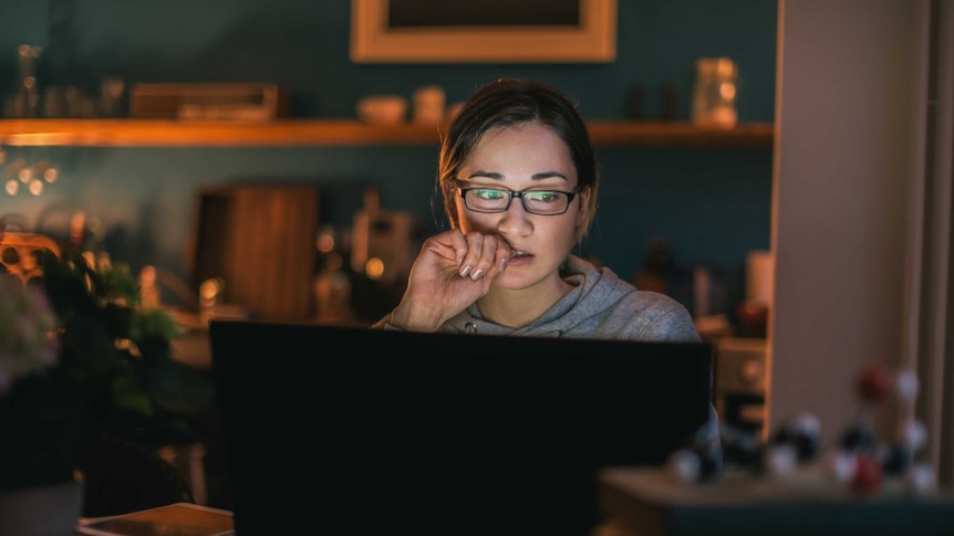 A young woman with glasses pensively staring at a computer.