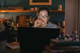 A young woman with glasses pensively staring at a computer.
