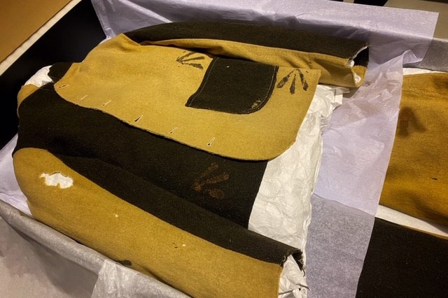 An historic yellow and black convict uniform worn in WA lies in a storage box with tissue paper underneath it.