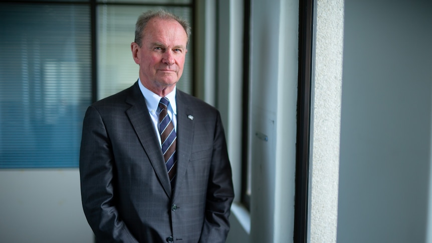 Man wearing a suit, standing next to a window.