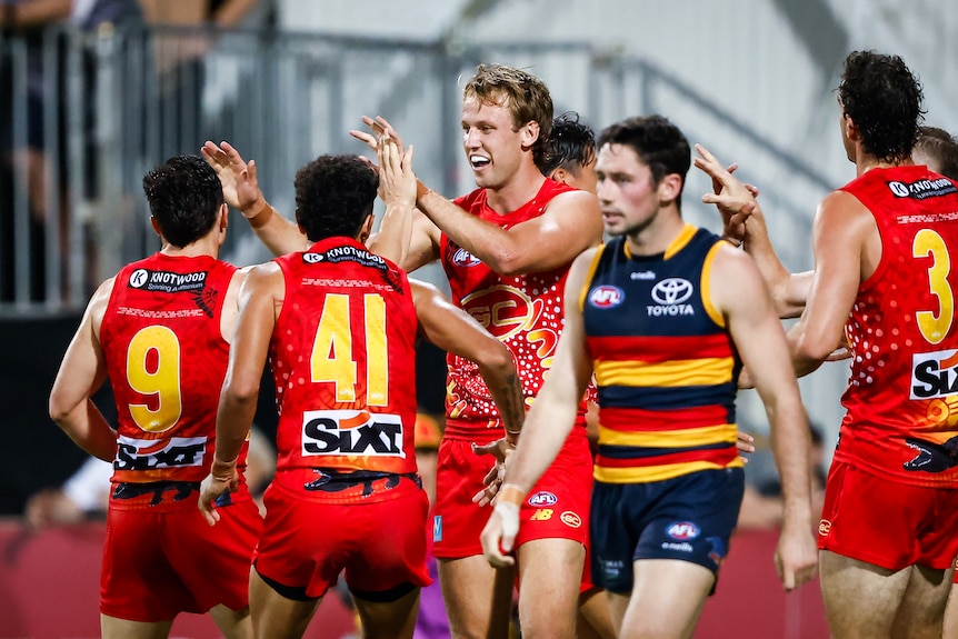 A Gold Coast AFL player gets a pat on the back from his teammates after kicking a goal.