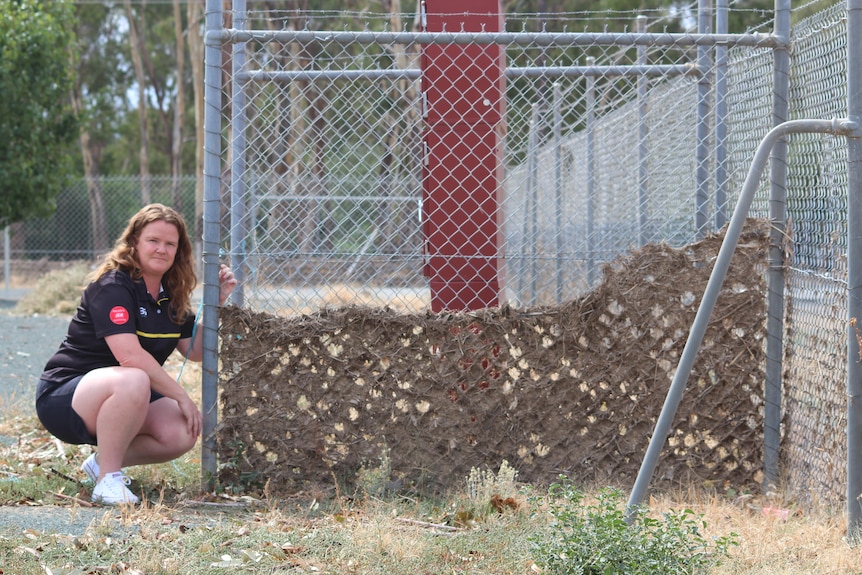 Katie Rasmussen kneels beside a fence full of debris from floods.