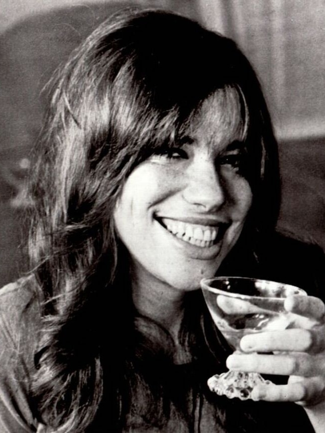 A young smiling woman salutes the camera with a glass