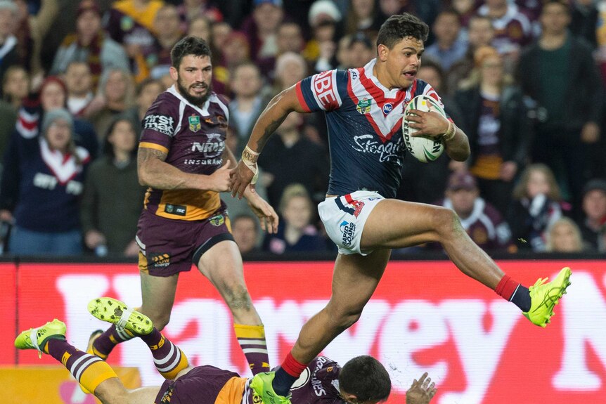 Latrell Mitchell runs with the ball for the Roosters as Ben Hunt dives in an attempt to make a tackle.