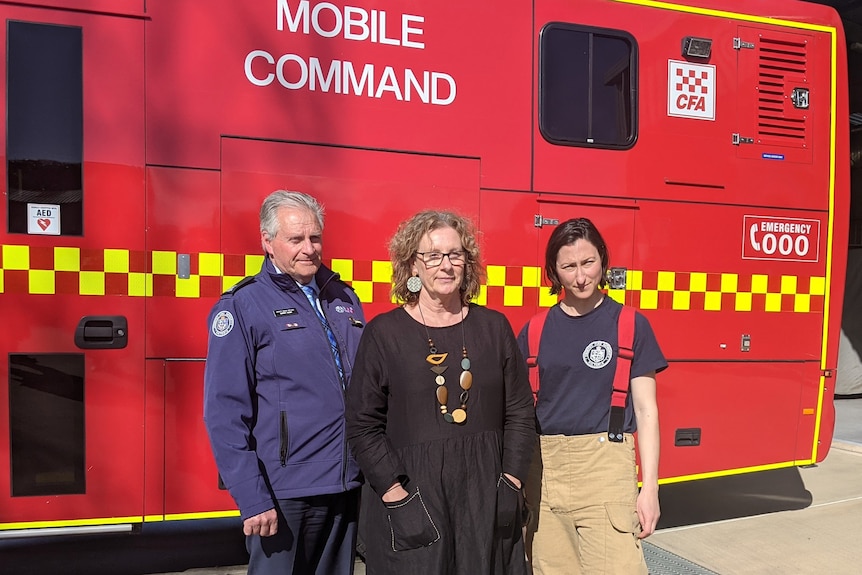 A man in CFA uniform stands with a woman in a black dress and a young woman in firefighter uniform in front of a fire truck