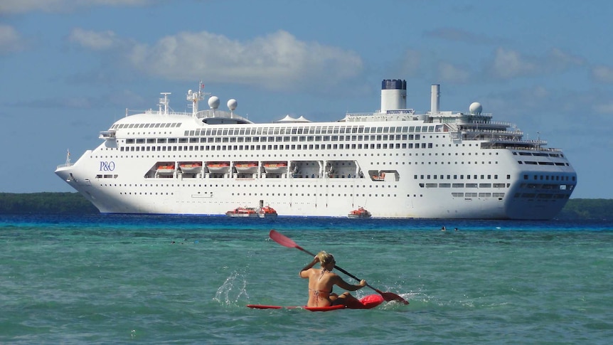 The Pacific Dawn looms large in the background, as someone paddles a canoe near the camera in the sea near Lifou island.