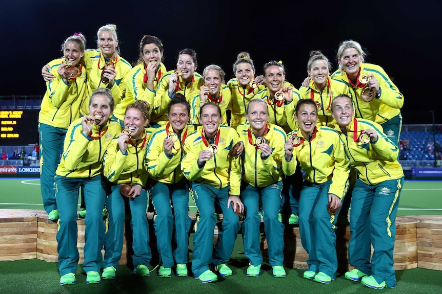 The Australian women's hockey team stands on the podium, holding their gold medals.